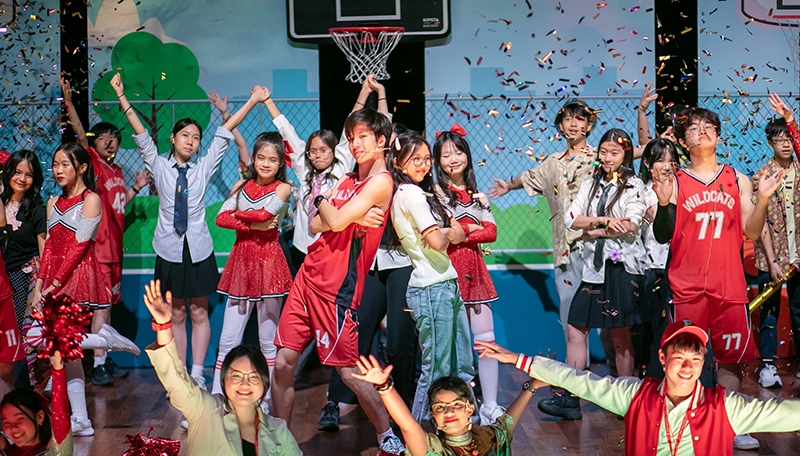 Students performing the final scene alongside the cast as confetti falls across the stage.